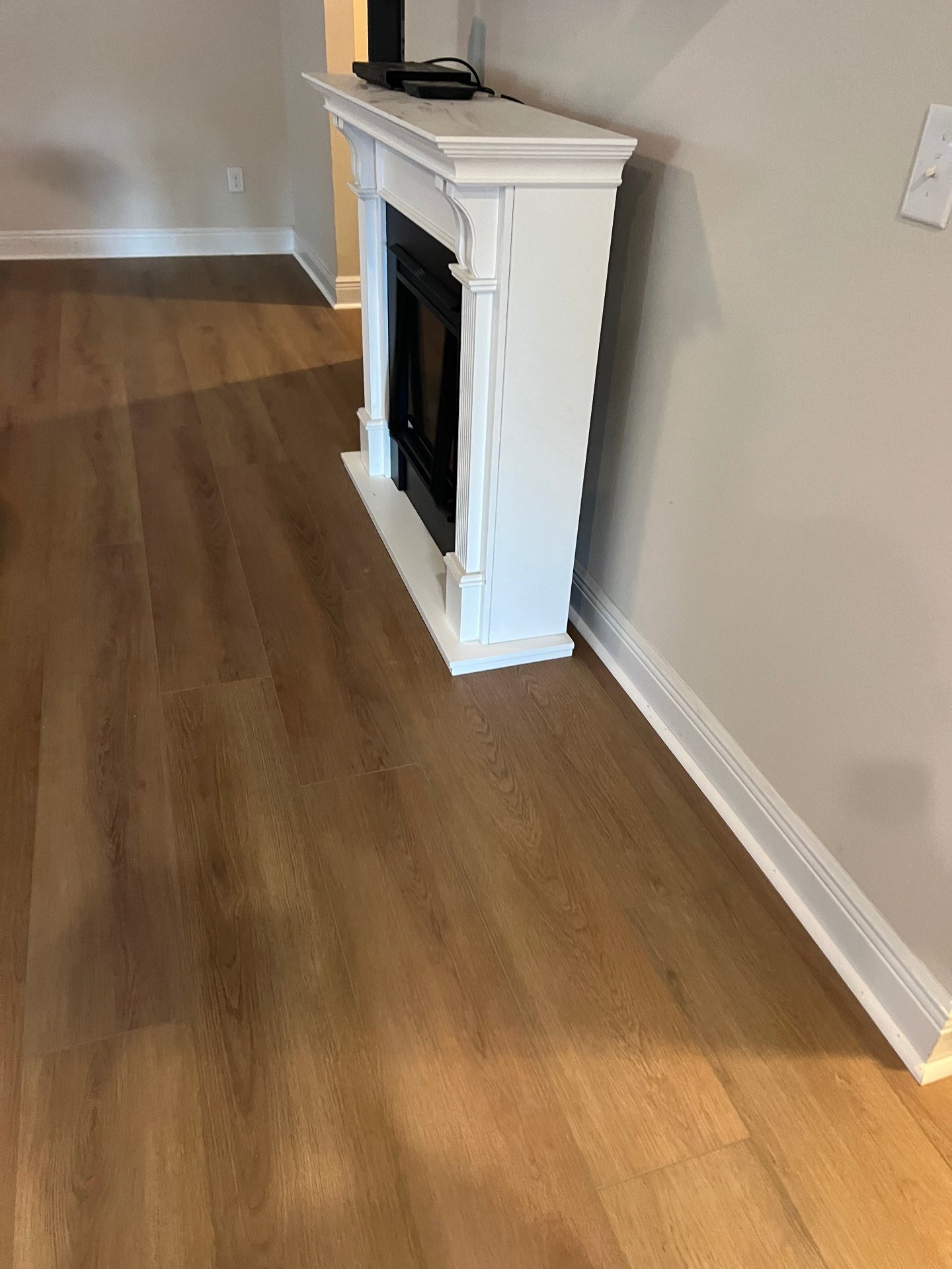 Living room vinyl plank flooring around white fireplace mantel featuring warm oak-tone luxury vinyl planks with seamless installation