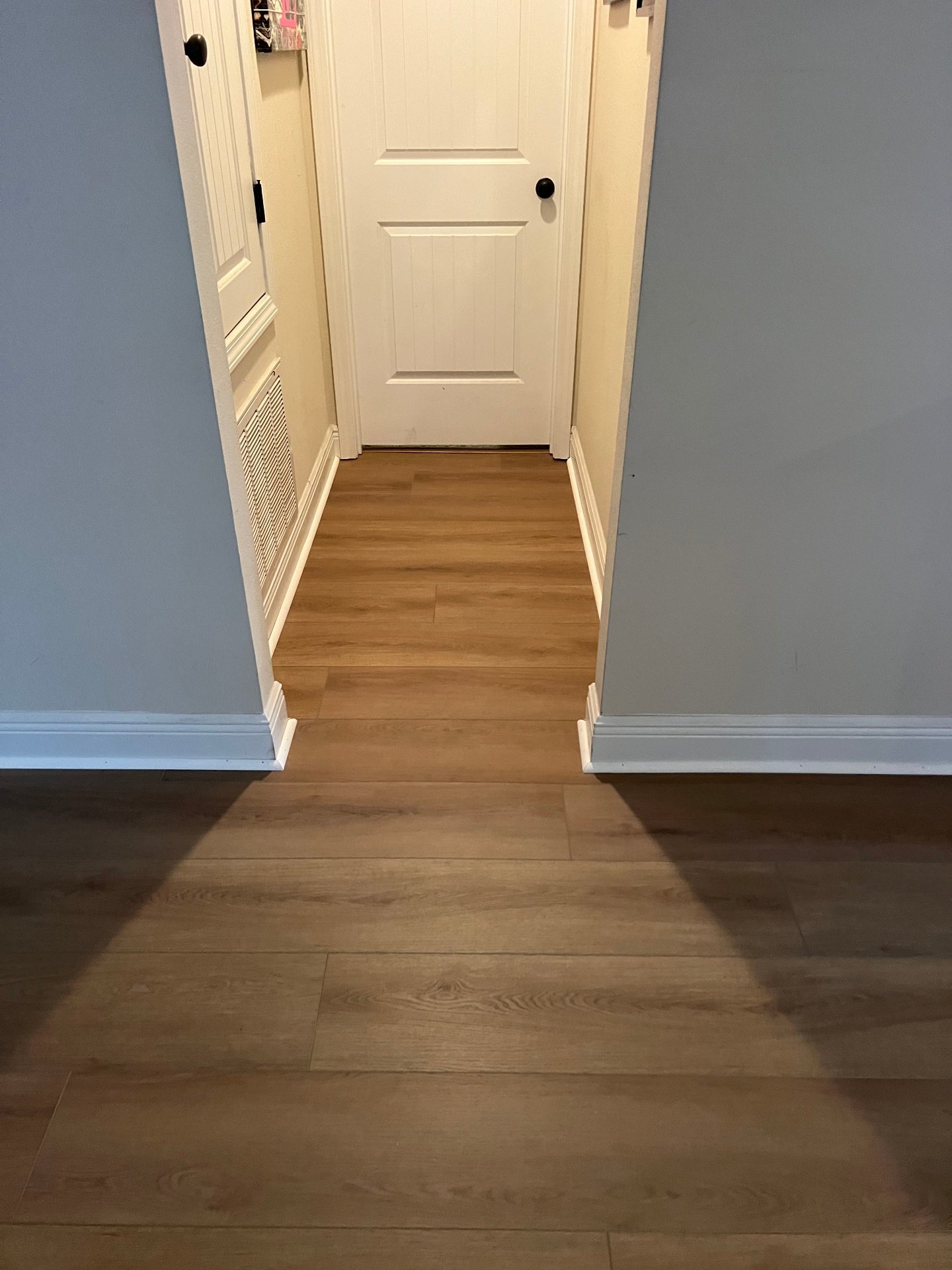Narrow hallway luxury vinyl plank installation with gray-blue walls and white trim featuring scratch-resistant LVP flooring