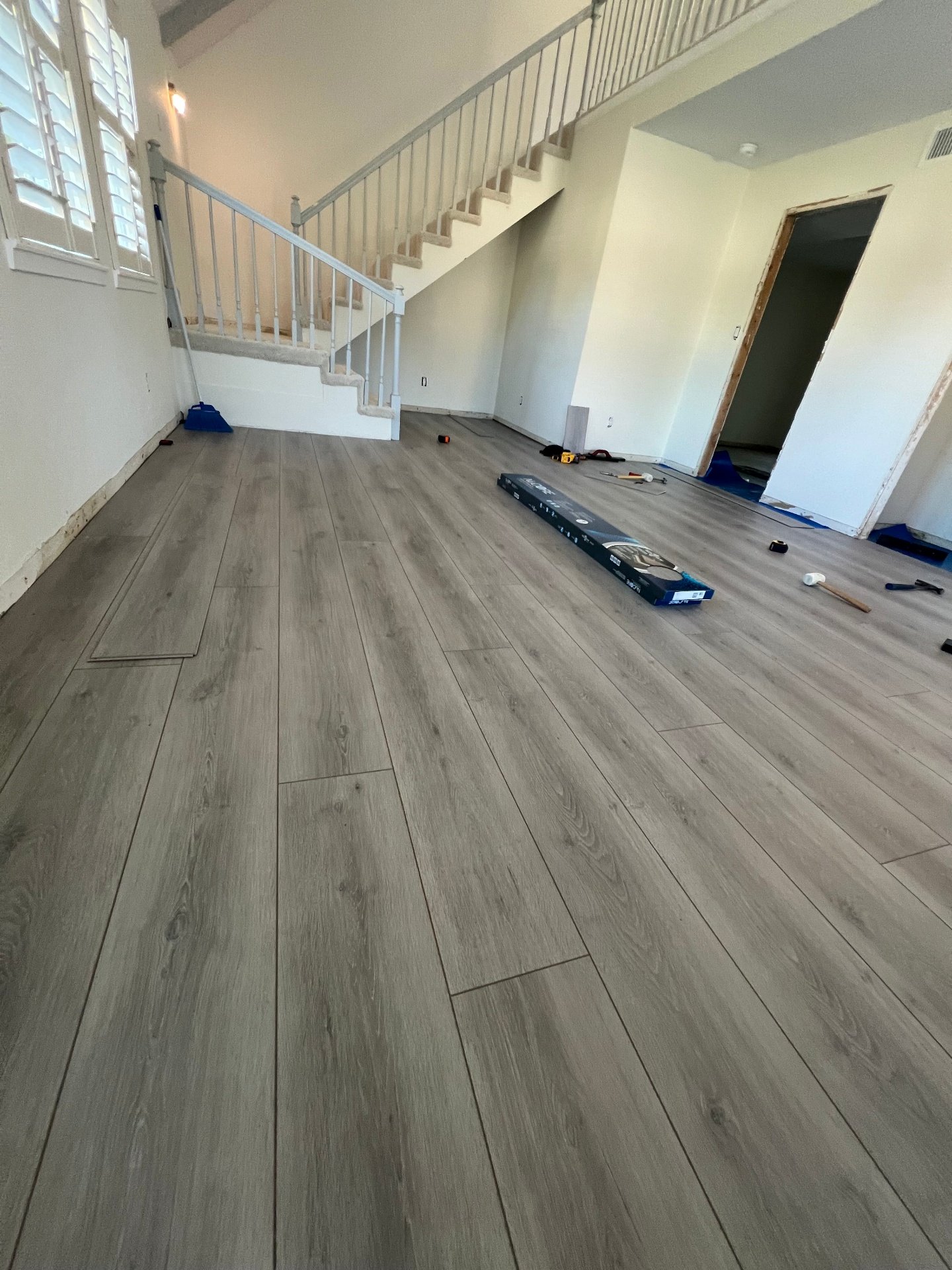 Two-story home vinyl plank installation near staircase showing professional flooring work with white railing and open layout